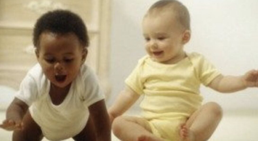 two cute babies, one is sitting, one is crawling