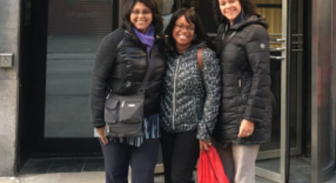 three women wearing winter coats and standing outside a building entrance