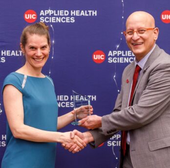 Image of Vera receiving the award and shaking hands with the AHS dean Carlos Crespo
                  